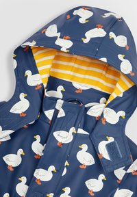 Marineblaue Regenjacke mit weißen Entenmuster, orangefarbenen Füßen und gelb gestreiftem Futter. Verfügt über eine Kapuze und sichtbare Klettverschlussdetails.