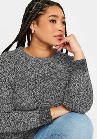 Grå stickad tröja med ett strukturerat mönster, rund halsringning och långa ärmar, kombinerad med ljusblå denim.