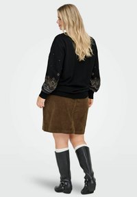 Melna sporta krekls ar rakstainām piedurknēm, pārī ar brūnu korduroja svārku. Modele valkā melnas ceļgalu augstās zābakus ar sprādzi.