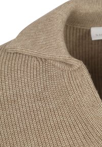 Beige gebreide trui met een geribbelde kraag en een opgevouwen ontwerp, dat een zachte, warme stof en subtiele kleurvariaties laat zien.