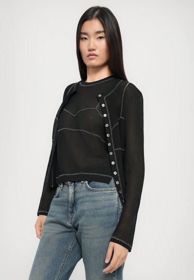 Top negru din tricot cu mâneci lungi și cusături albe contrastante. Prezintă un închizător cu nasturi mari și o croială relaxată.