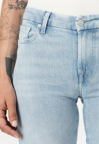 Jeans en denim bleu clair avec une coupe droite, dotés d'une poche avant, d'une fermeture à bouton argenté et d'un léger effet de décoloration.