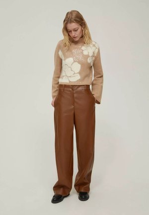 Maglione beige lavorato a maglia con design floreale, abbinato a pantaloni in pelle marrone a gamba larga. Fit rilassato e testurizzato, con una leggera lucentezza sul maglione.