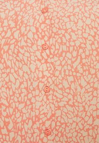 Chemise à boutons avec un motif abstrait corail et crème. Présente cinq boutons ronds corail le long du centre et une texture de tissu lisse.