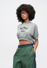 Γκρι κοντό φούτερ με μαύρη εκτύπωση "NIKE 1972", συνδυασμένο με πράσινο αθλητικό παντελόνι με μπλε σκούρα μέση και λογότυπο Nike.