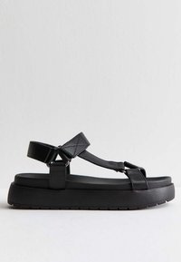 Svarta plattformssandaler med en tjock sula, breda remmar och t-bar-design. Tillverkade av ett slätt material med en matt textur.