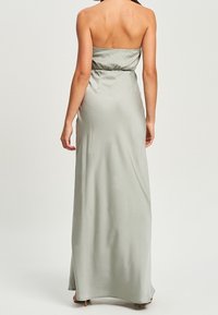 Eine Frau steht mit sichtbarem Rücken und trägt ein langes, trägerloses, hellgraues Satinkleid mit taillierter Taille und bodenlangem Saum.