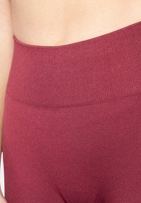 Leggings bordeaux taille haute avec une ceinture côtelée et une texture lisse, conçus pour le confort et la flexibilité.