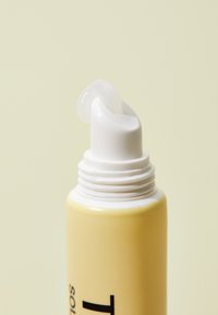 Gul tube med hvid dyse, der dispenserer en klar gel. Designet er glat med minimal tekst. Baggrunden er i en blød, afdæmpet farve.