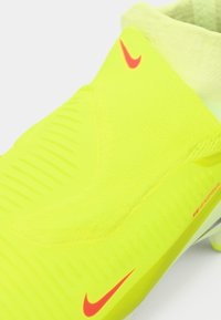 Fényes sárga sportcipő, illeszkedő, texturált felsőrésszel és sima talppal. Piros Nike logóval és kiemelkedő bordázott részletekkel rendelkezik.