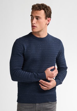 Navy-blauwe gebreide trui met een textuurpatroon, ronde hals en ribgebreide manchetten. Slanke pasvorm met subtiele kleurvlekken.