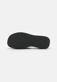 Suela de zapato negra con una superficie texturizada, que presenta una forma redondeada y un sutil detalle de marca. Material suave y flexible.