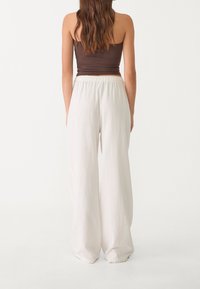 Bílé kalhoty s širokými nohavicemi vyrobené z lehké látky s elastickým pasem, zkombinované s těsným hnědým topem, pohled zezadu.