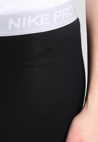 Leggings neri realizzati con materiale liscio ed elastico, dotati di una fascia elastica bianca in vita con la scritta "NIKE PRO". Vista ravvicinata del tessuto e della vestibilità.