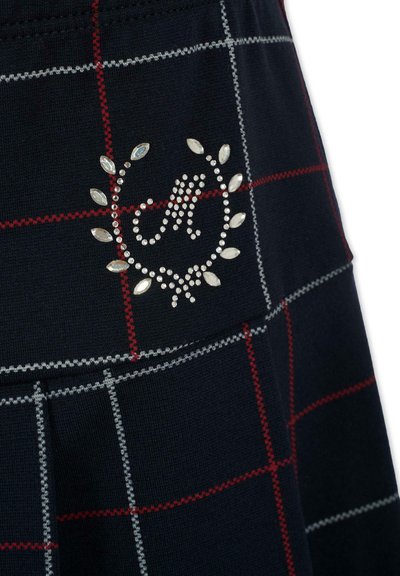 Jupe marine à motif tartan rouge et gris. Présente un logo décoratif avec des strass entouré d'un design circulaire.