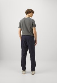 Un t-shirt gris à manches courtes, un pantalon élastique bleu marine et des baskets de couleur claire. Le t-shirt présente un logo discret au dos.