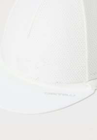 Hvit sykkelhatt laget av teksturert stoff med ventilert design. Har en myk skjerm og en logo trykt på forsiden.