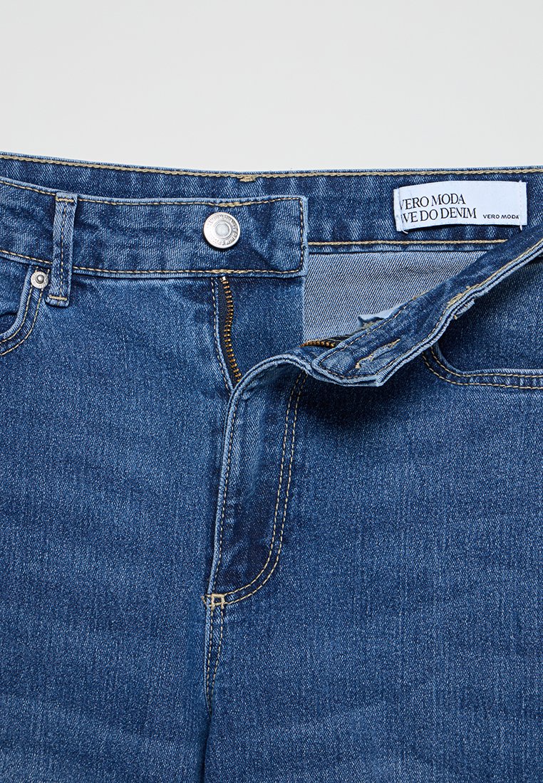 Dunkelblaue Jeans aus Denim mit einem genähten Bund, metallischem Verschluss, Reißverschluss und VERO MODA-Label innen. Glatte Textur und klassisches Design.