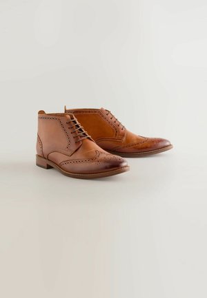 Ruske nahkasaapad sievitettyjen brogue-yksityiskohtien kanssa, joissa on pyöreä kärki, nauhakiinnitys ja matala pinottu korko. Liukas pinta.