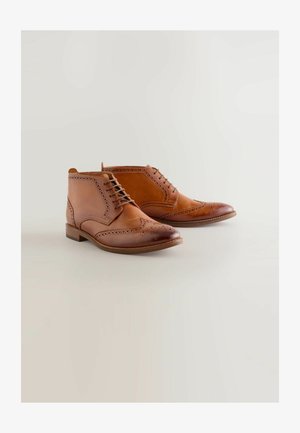 Hnedé kožené členkové topánky s brogue detailmi, s okrúhlou špičkou, šnurovaním a nízkym zloženým podpätkom. Hladký povrch.