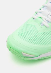 Baskets de sport vert clair avec une tige en maille texturée, lacets blancs et semelle rembourrée. Présente un bout arrondi et des éléments de design minimalistes.