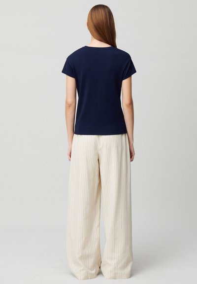 T-shirt blu navy a maniche corte con scollatura rotonda, abbinato a pantaloni a gamba larga color crema con sottili righe verticali.