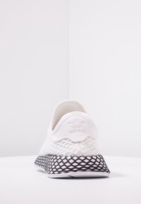 Vita mesh sneakers med en texturerad svart gummisula, med en logotyp på hälen och en slip-on-design för enkel på- och avtagning.