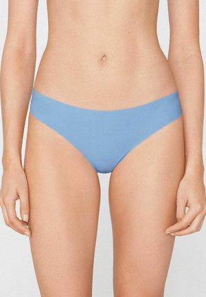 Frau trägt nahtlose hellblaue Bikini-Unterwäsche, dargestellt von der Taille bis zu den oberen Oberschenkeln vor einem schlichten Hintergrund.