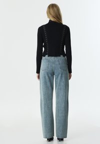Col roulé noir à côtes avec des clous métalliques sur les côtés, associé à un jean bleu clair à jambe large avec poches arrière.