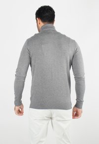 Pull gris à manches longues avec un col montant. Le tissu semble lisse avec une coupe ajustée. Pas de motifs visibles ni de détails en métal.