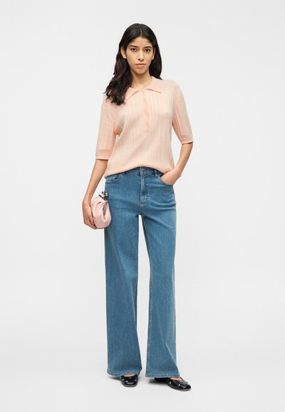 Ανοιχτό ροδακινί πόλο μπλουζάκι με ριμπ ύφασμα και κοντά μανίκια, συνδυασμένο με παντελόνι τζιν φαρδύ και ψηλόμεσο σε ανοιχτό γαλάζιο χρώμα και μια μικρή ροζ τσάντα χειρός.