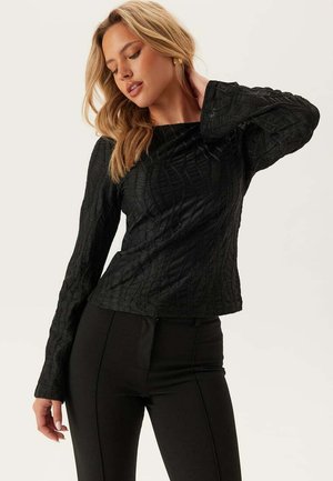 Zwart langemouwen top met textuurpatroon, lichte bootnek en uitlopende mouwen, gecombineerd met zwarte fitted pants.