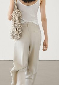 Light gray wide-leg trousers with a smooth texture, paired with a white sleeveless top and a textured fringe shoulder bag.