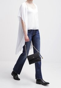 Kimono blanco fluido con encaje en los bordes, combinado con una camiseta blanca y jeans azul oscuro. Un bolso negro con cadena y botas de tobillo completan el atuendo.