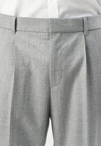 Gray tailored formal trousers with belt loops worn with a tucked-in white shirt, highlighting the waist and front seam details.