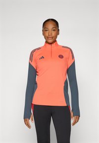 Long-sleeve athletic top in bright coral with gray accents. Features a half-zip collar and three horizontal stripes on shoulders.