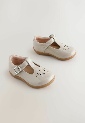 Fényes bézs T-bar cipők perforált virágmintával, ezüst csattal rögzítve. Puha rózsaszín bélés és rugalmas barna gumi talp.