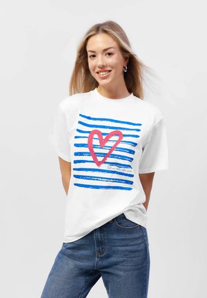 T-shirt en coton blanc avec un design de cœur rose et de rayures bleues, avec le texte "Aime comme la mer." Coupe décontractée avec des manches courtes.