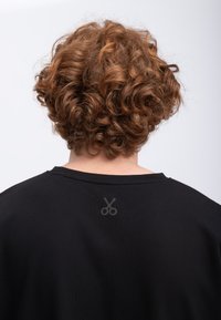 T-shirt noir à col rond, avec un graphique de ciseaux gris au dos. Le tissu semble texturé avec une coupe décontractée.