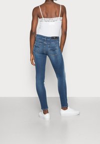 Jeans de denim azul ajustados con cintura de altura media, bolsillos traseros con costuras curvadas y combinados con zapatillas blancas.