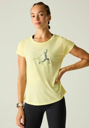 Woman with braided hair wearing a yellow t-shirt with yoga pose graphics and black leggings, standing with one hand on her hip.
