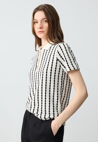 Polo à manches courtes en crème avec des rayures verticales noires, présentant une patte de boutonnage et un col côtelé, détail de tissu texturé.