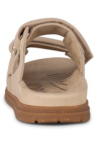 Beige sandal med en texturerad sula, justerbar rem och gummisula. Baksidan är öppen med en vadderad foder och inga utsmyckningar.