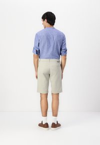 Lys blå skjorte med lange ermer og beige shorts. Skjorten har oppbrettede ermer; shortsen har en baklomme. Brune sko og hvite sokker synlige.
