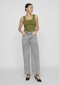 Top senza maniche verde oliva abbinato a jeans grigi a vita alta e gamba larga, con una leggera scoloritura. Il modello indossa tacchi a punta neri.