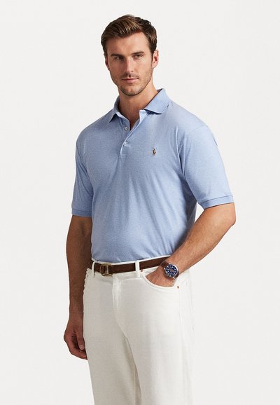 Γαλάζια πόλο μπλούζα με κλασικό γιακά, τρεις κουμπότρυπες και μικρό κεντητό λογότυπο στο αριστερό στήθος. Φορεμένη με λευκά παντελόνια.