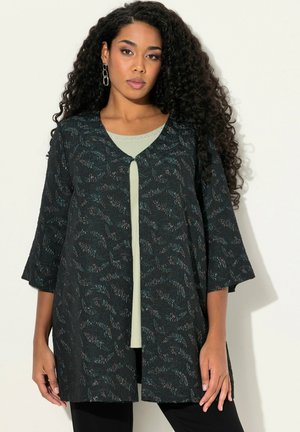 Schwarz gemusterte Jacke mit V-Ausschnitt, mit 3/4-Ärmeln. Über einem hellgrünen Oberteil getragen. Glatte Textur mit einem floralen Designelement.