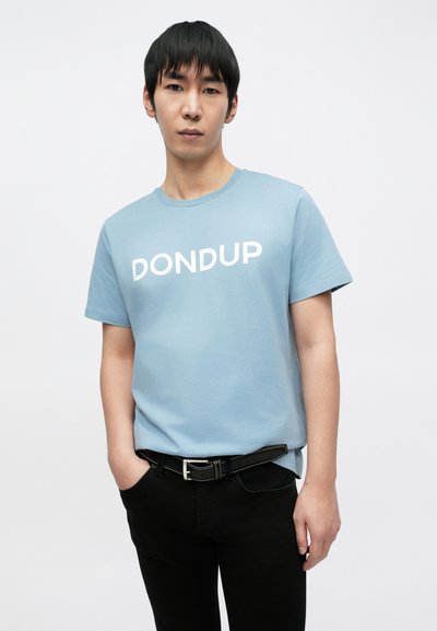 Ανοιχτό μπλε βαμβακερό μπλουζάκι με λευκή επιγραφή "DONDUP", συνδυασμένο με μαύρο παντελόνι και μαύρη ζώνη. Απλός στρογγυλός λαιμός και κοντά μανίκια.