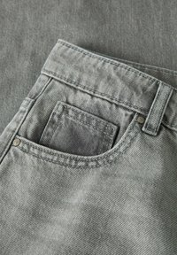 Acercamiento a un bolsillo de unos pantalones vaqueros de mezclilla gris que muestra las costuras, remaches, el lazo del cinturón y un bolsillo interior más pequeño.