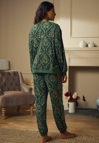 Set de îmbrăcăminte de lounge cu model florar verde, realizat dintr-un material moale, având manșete și margine elastice. Croială lejeră cu imprimeu botanic detaliat.